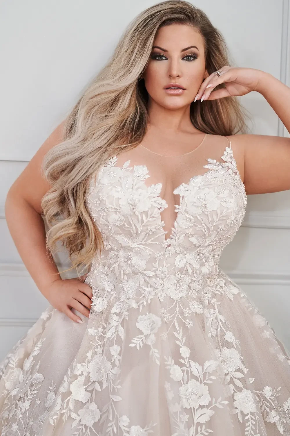 A woman wearing a beautiful, embellished wedding dress with a deep V-neckline and floral appliqu&eacute;s.