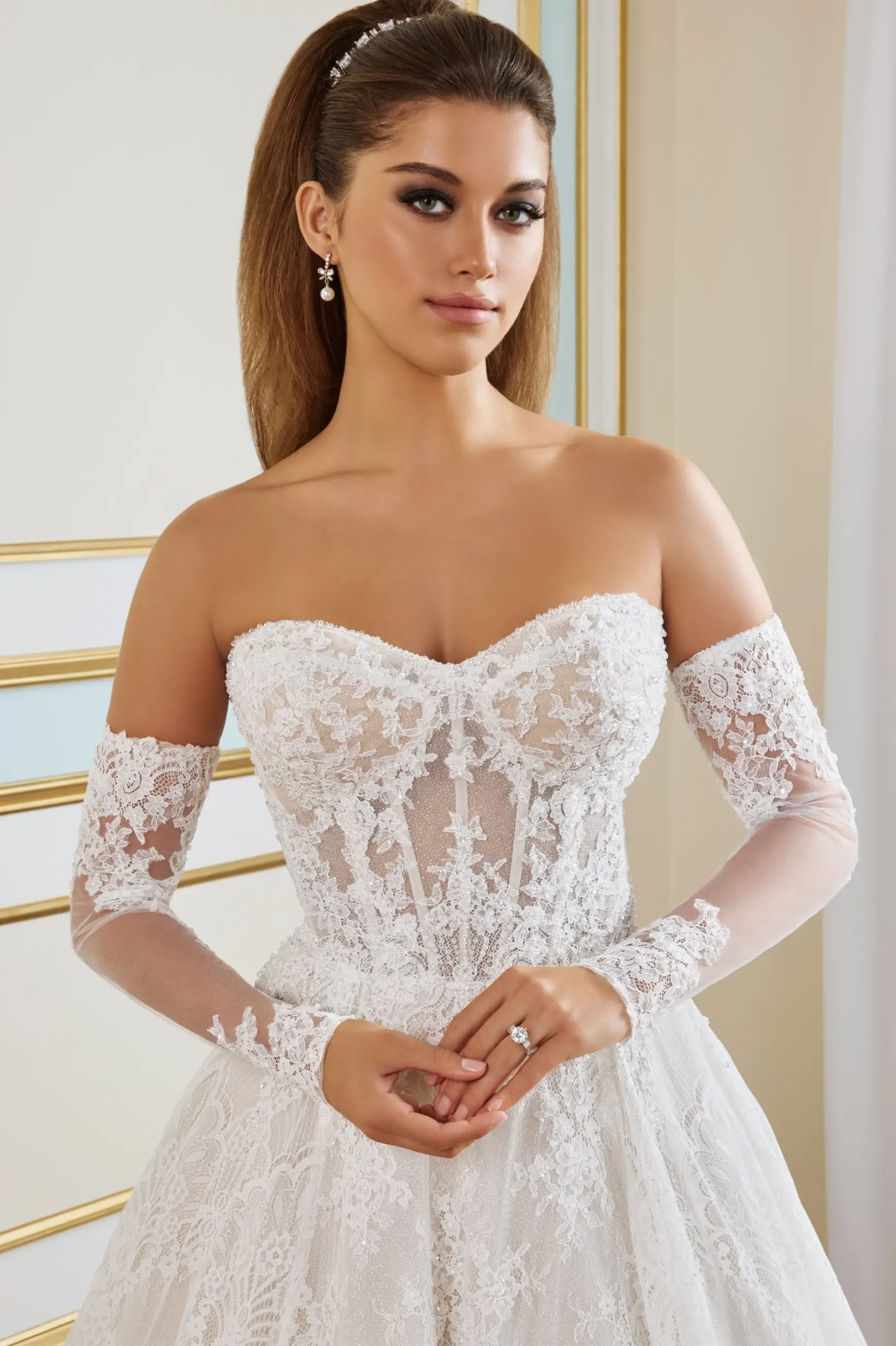 Model is wearing an A-line wedding gown with a sweetheart neckline, corded Chantilly lace, glitter tulle layers, a dramatic train, and separate long semi-sheer illusion sleeves.