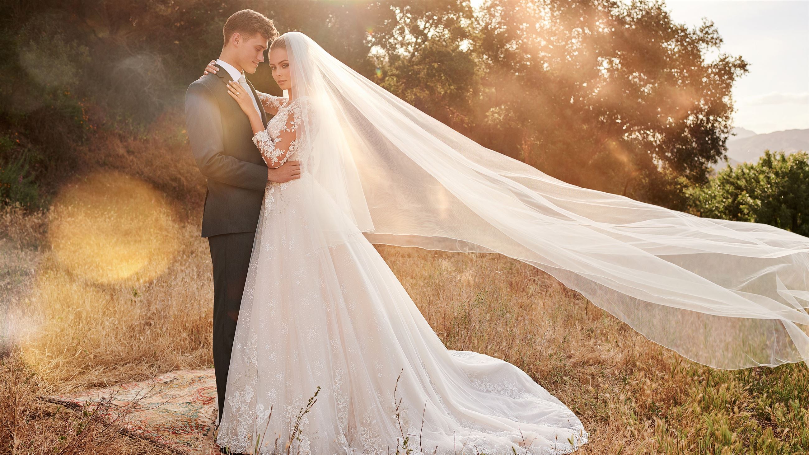 Bride and groom holding each other with bride's veil blowing in wind