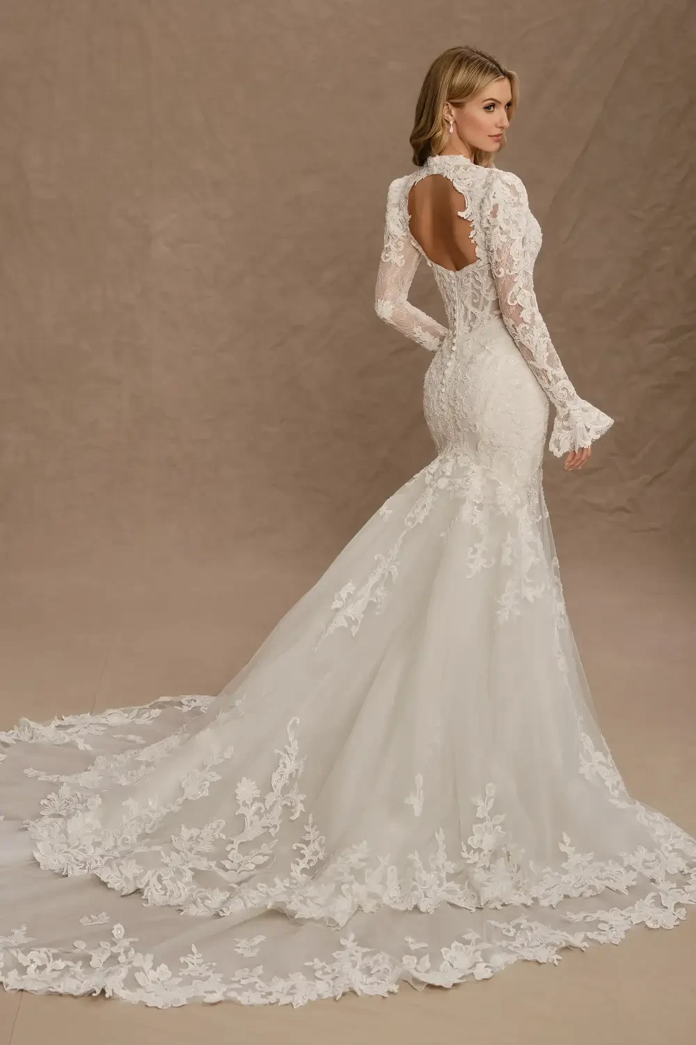 A beautiful bride wearing a fitted, lace wedding gown with long sleeves and an elegant train, standing in a beautifully lit setting with intricate background details.