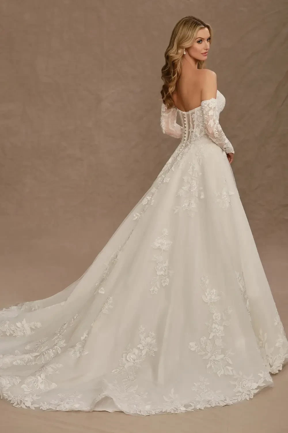 A woman in a strapless, white wedding dress twirls, showcasing the gown's full skirt and intricate lace details. She wears matching white gloves and appears joyful, with a softly lit, elegant background.