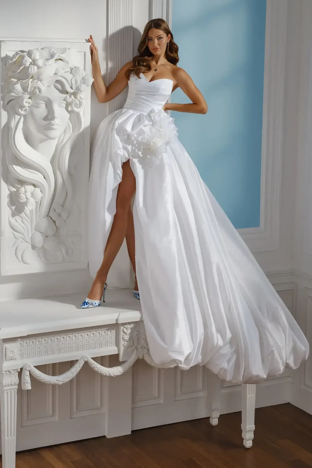 model is wearing a sleeveless bridal gown with a high low slit