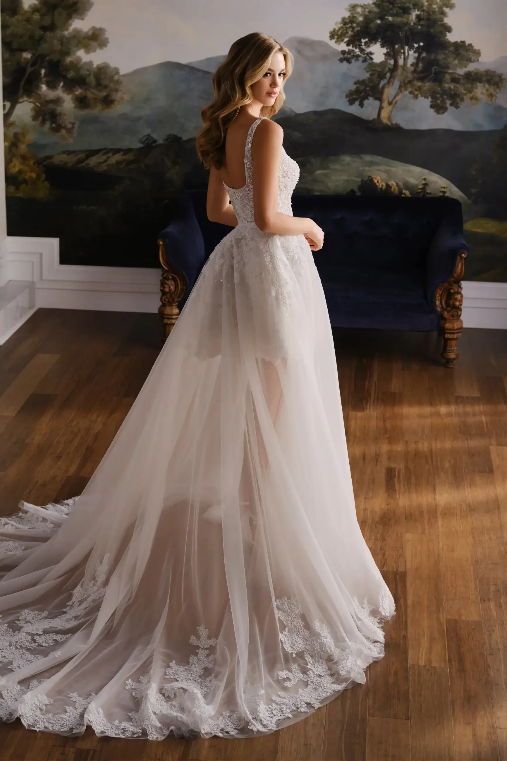 Model is wearing a short lace bridal dress with a square neckline and detachable overskirt for added versatility.