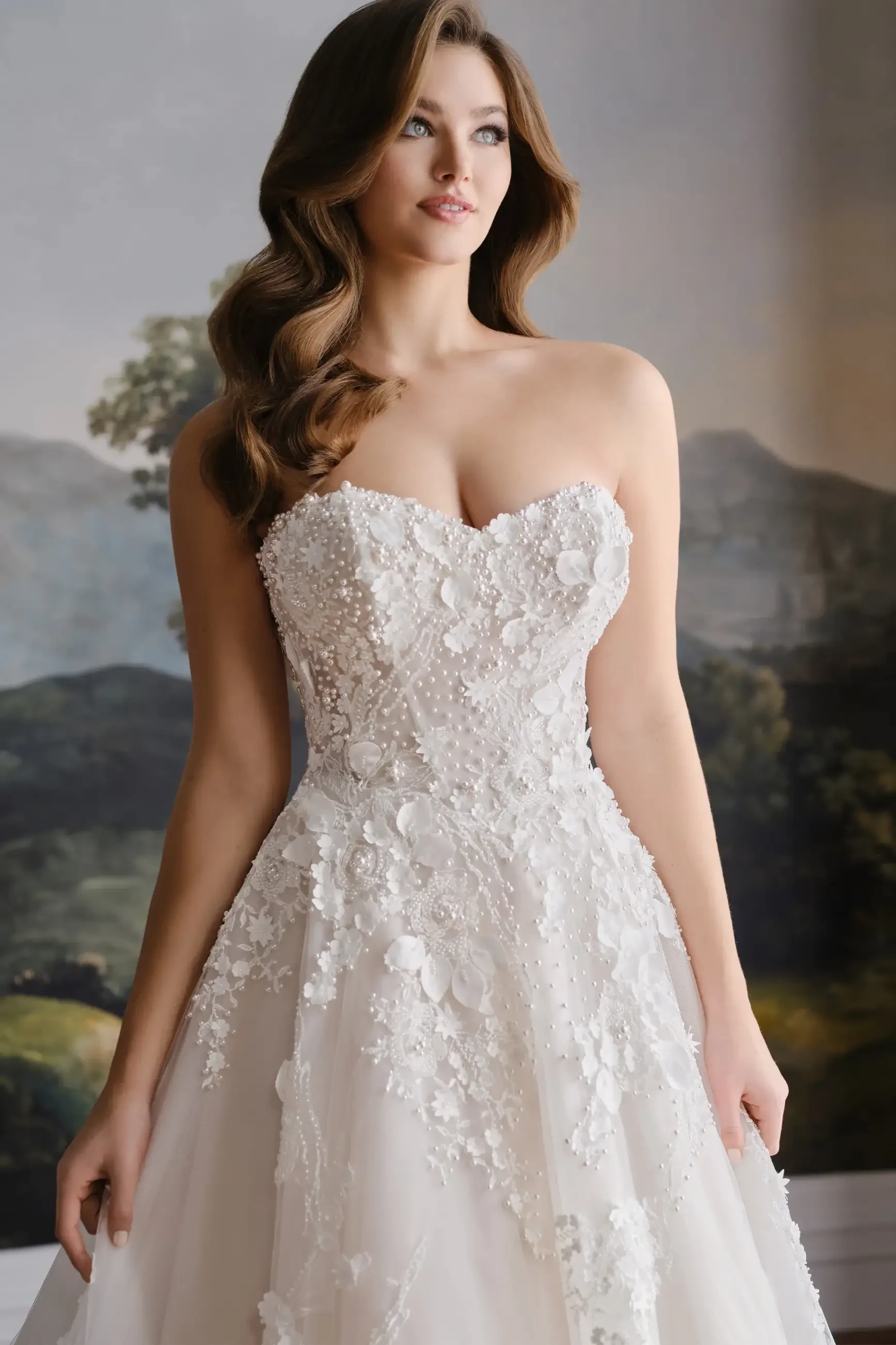 Model is wearing a strapless organza ball gown with a sweetheart neckline and removable pearl-beaded straps.
