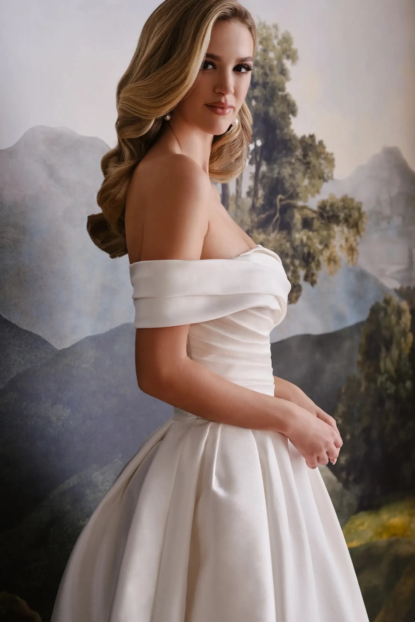 Model is wearing a mikado and organza bridal gown with a sculpted neckline