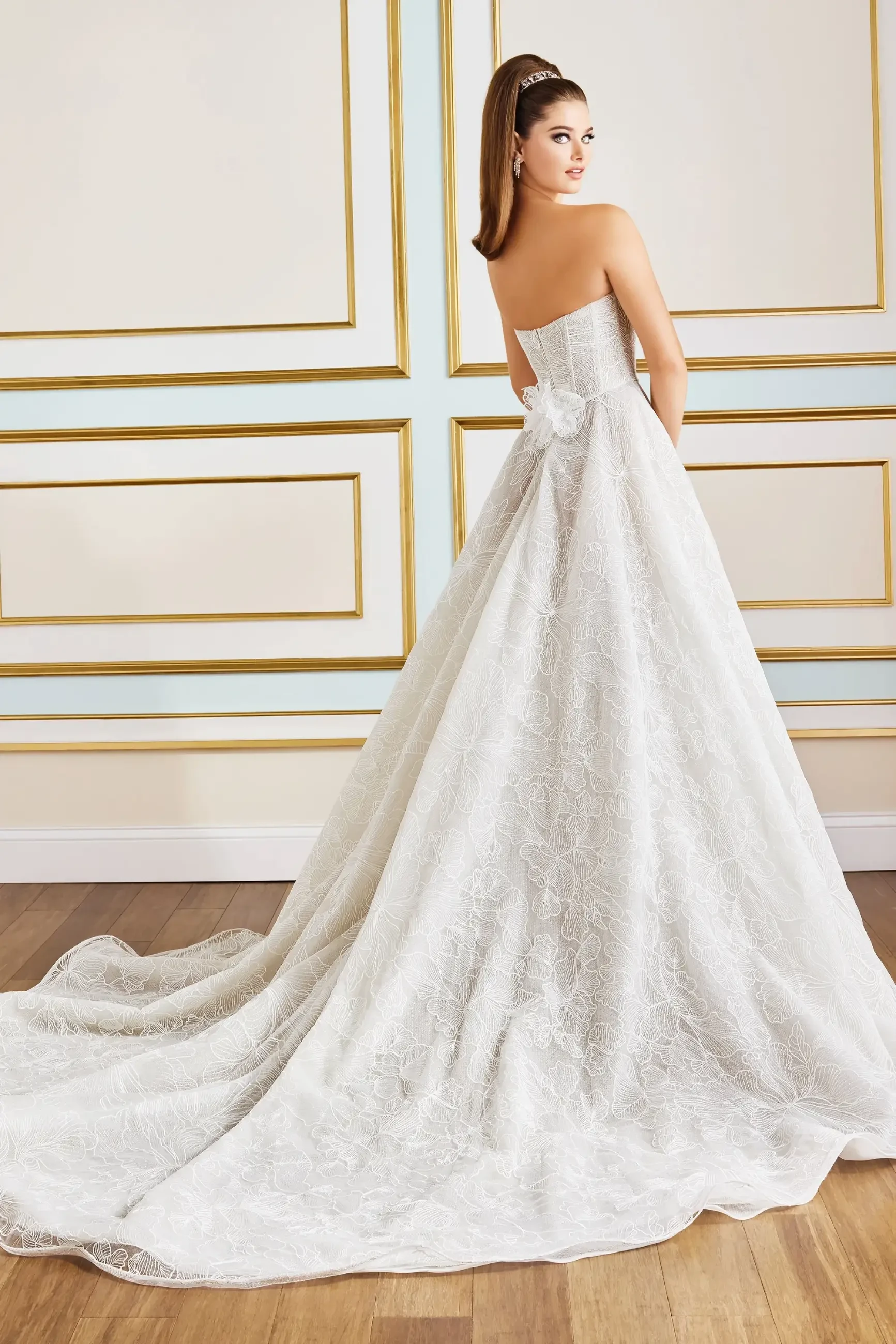Model is wearing a strapless A-line gown with a sweetheart neckline, floral embroidered tulle, and a high slit, available in ivory or black.