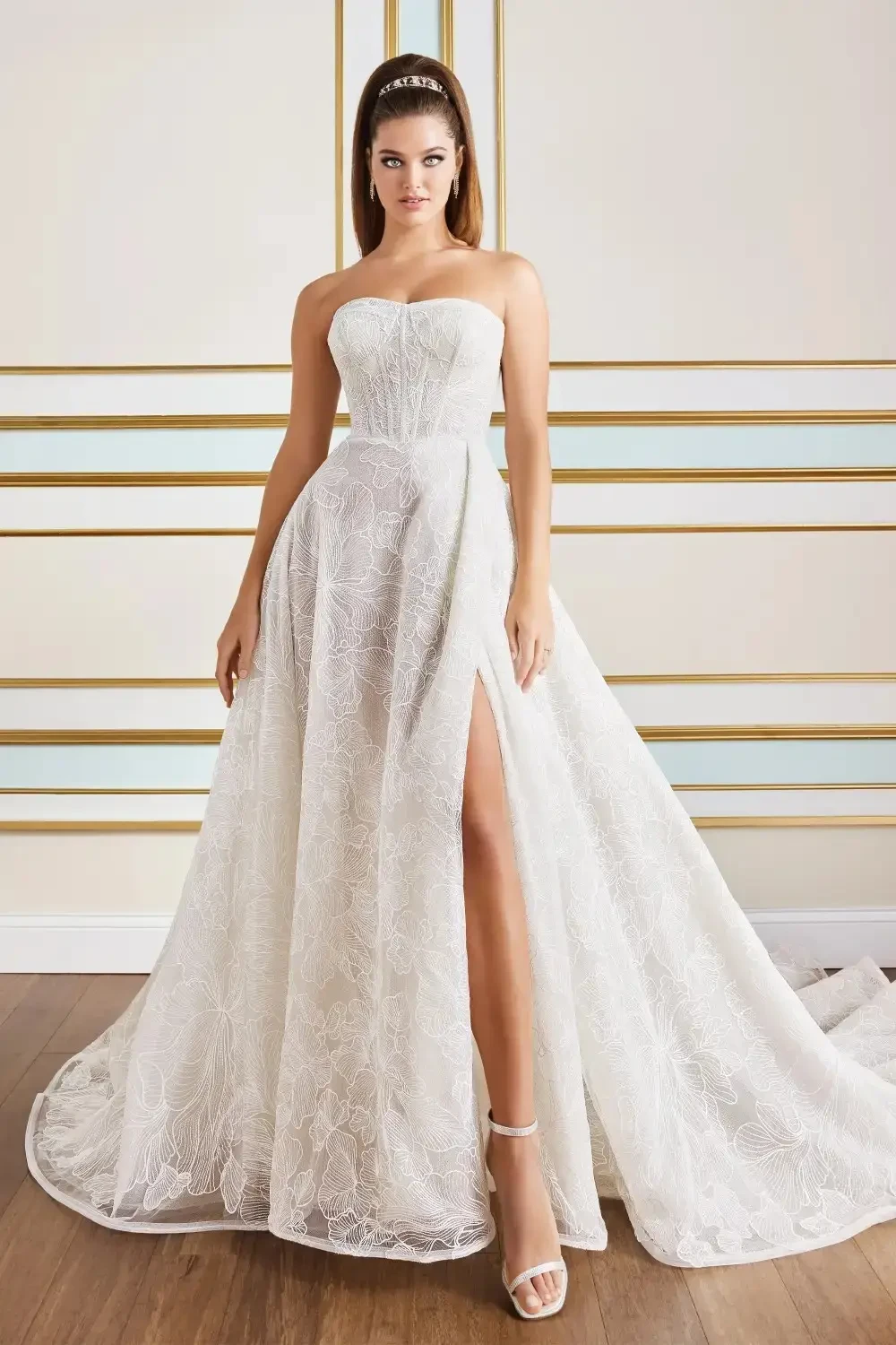 Model is wearing a strapless A-line gown with a sweetheart neckline, floral embroidered tulle, and a high slit, available in ivory or black.