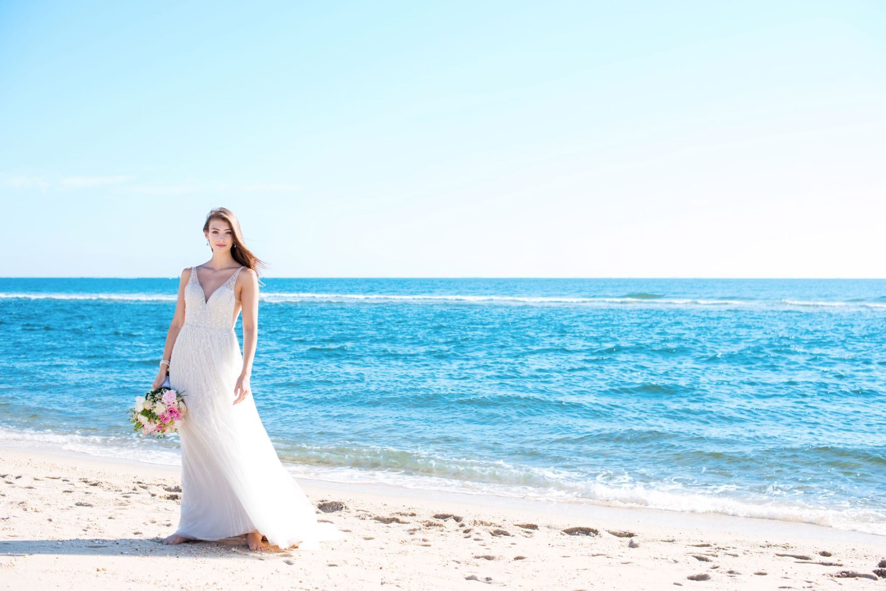 Brunette model on beach holding flowers and wearing wedding dress